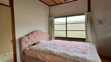 Une chambre avec un lit rose, un plafond en bois, une fenêtre avec des rideaux et une porte coulissante de style japonais traditionnel.
