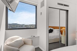 Ein Hotelzimmer mit Bett, Stuhl, Fenster und Stadtblick sowie einer Schiebetür zum Schrank.