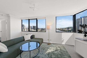 Ein modernes Wohnzimmer mit einem grünen Sofa, einem Glastisch und Blick auf eine Stadtlandschaft durch große Fenster.