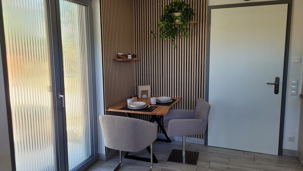 Een moderne eethoek met een tafel voor twee personen, een schuifdeur van glas, een verticaal gestreepte muur en een klok.