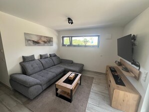 A modern living room with a grey sectional sofa, a wooden coffee table, a mounted flat-screen TV, and a small wooden cabinet.