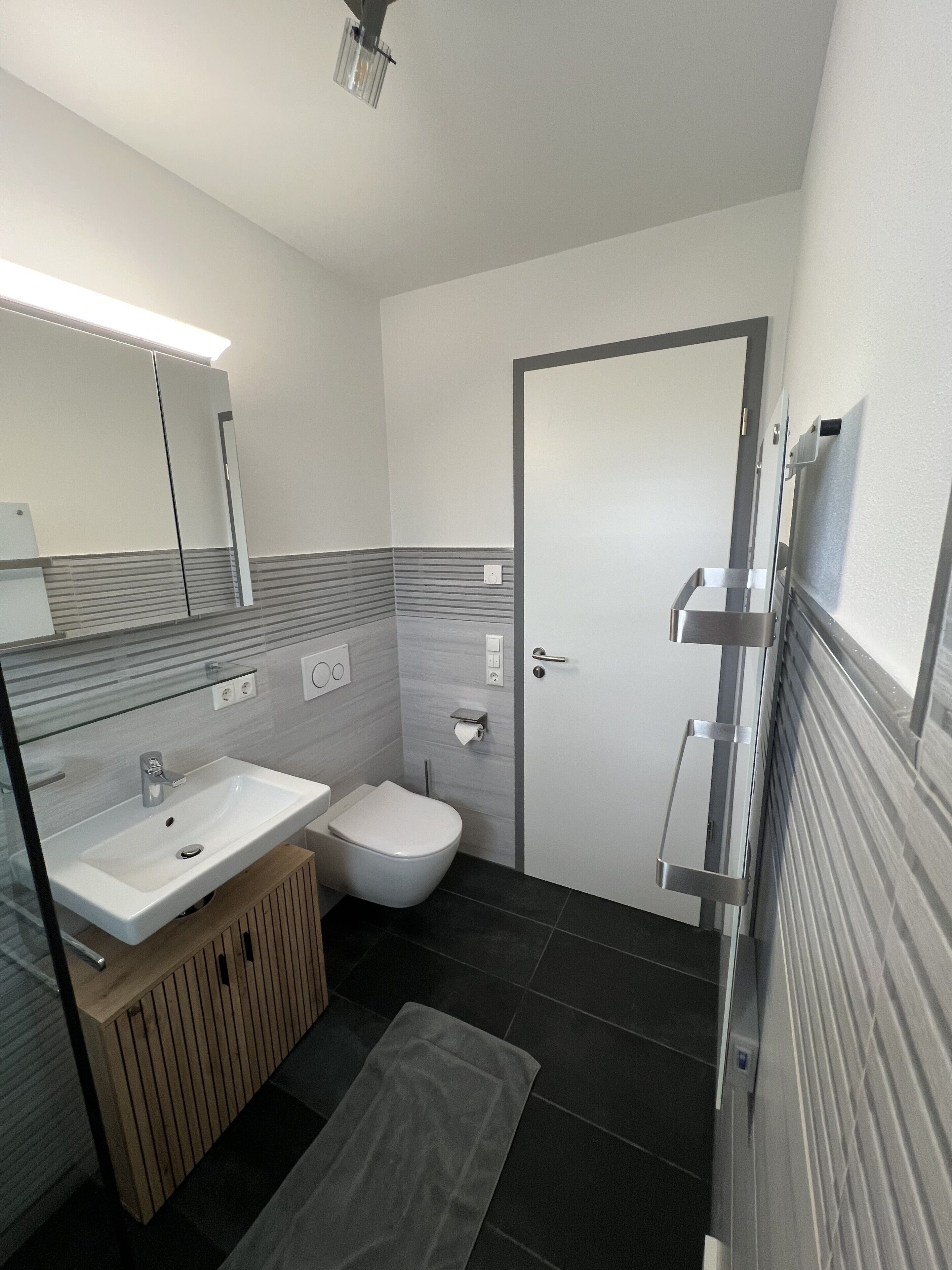 Een moderne badkamer met een witte wasbak, toilet en spiegel.