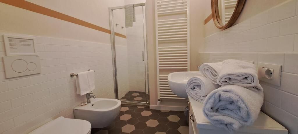 Un baño con inodoro, bidé, ducha y una pila de toallas.
