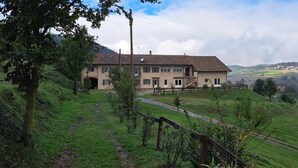 A two-story house with a paved driveway, surrounded by lush green fields and hills.