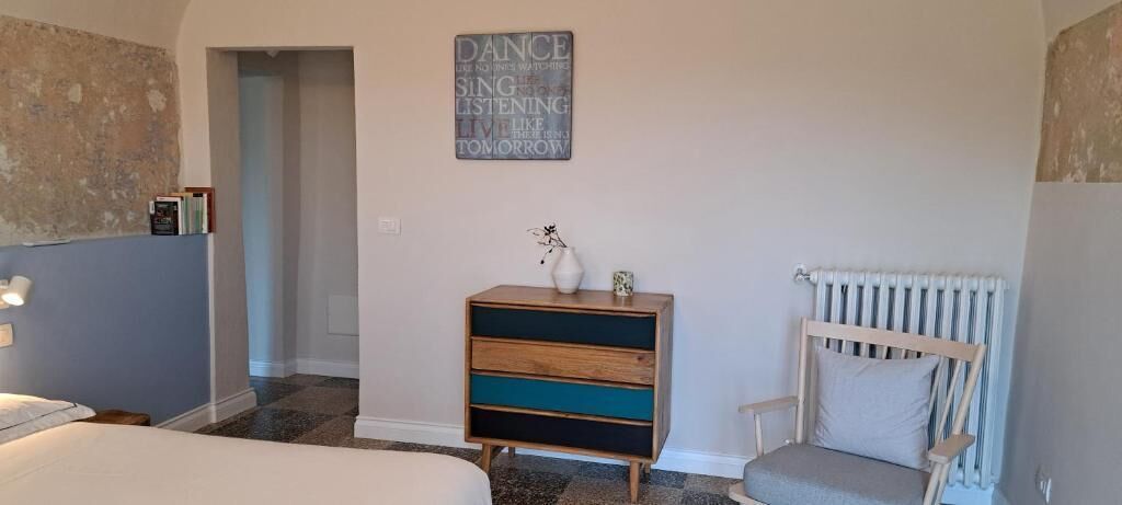 Ein Schlafzimmer mit Bett, Schminktisch, Stuhl, Heizkörper und einer Wand mit einem Motivationsspruch.