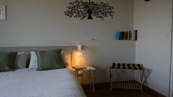 Een slaapkamer met een bed, kussens, een nachtkastje met een lamp, een kleine houten stoel, een boekenplank en een decoratie aan de muur.