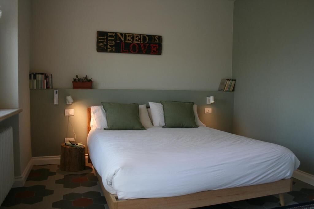 Una cama bien hecha con almohadas, un cartel en la pared y una mesita de noche con una lámpara.