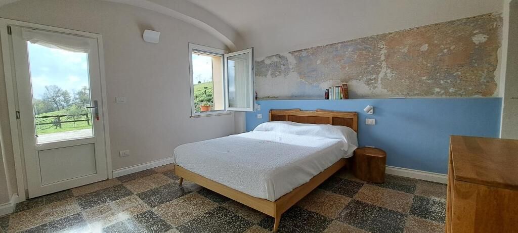 Une chambre à coucher avec un lit, une tête de lit en bois, une fenêtre, une porte et un sol à carreaux.