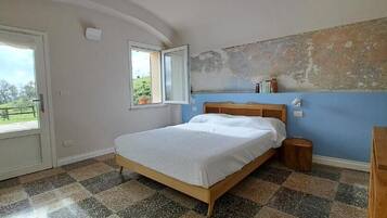 Un dormitorio con cama, cabecera de madera, ventana, puerta y suelo de cuadros.