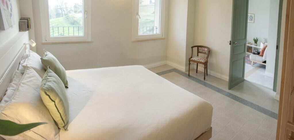 Une chambre à coucher avec un lit, des oreillers, une chaise et une vue sur un balcon.