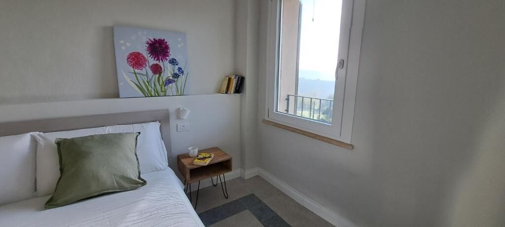 Ein Schlafzimmer mit Bett, Nachttisch, Fenster und einem Bild an der Wand.