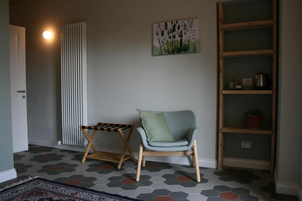 Ein Zimmer mit einem Sessel, einem kleinen Tisch, einer Heizung, einem Bücherregal und einem fußbodenhohen Hexagonmuster.