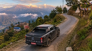 A black Ford Ranger truck on a winding mountain road with a view of a valley and distant mountains.