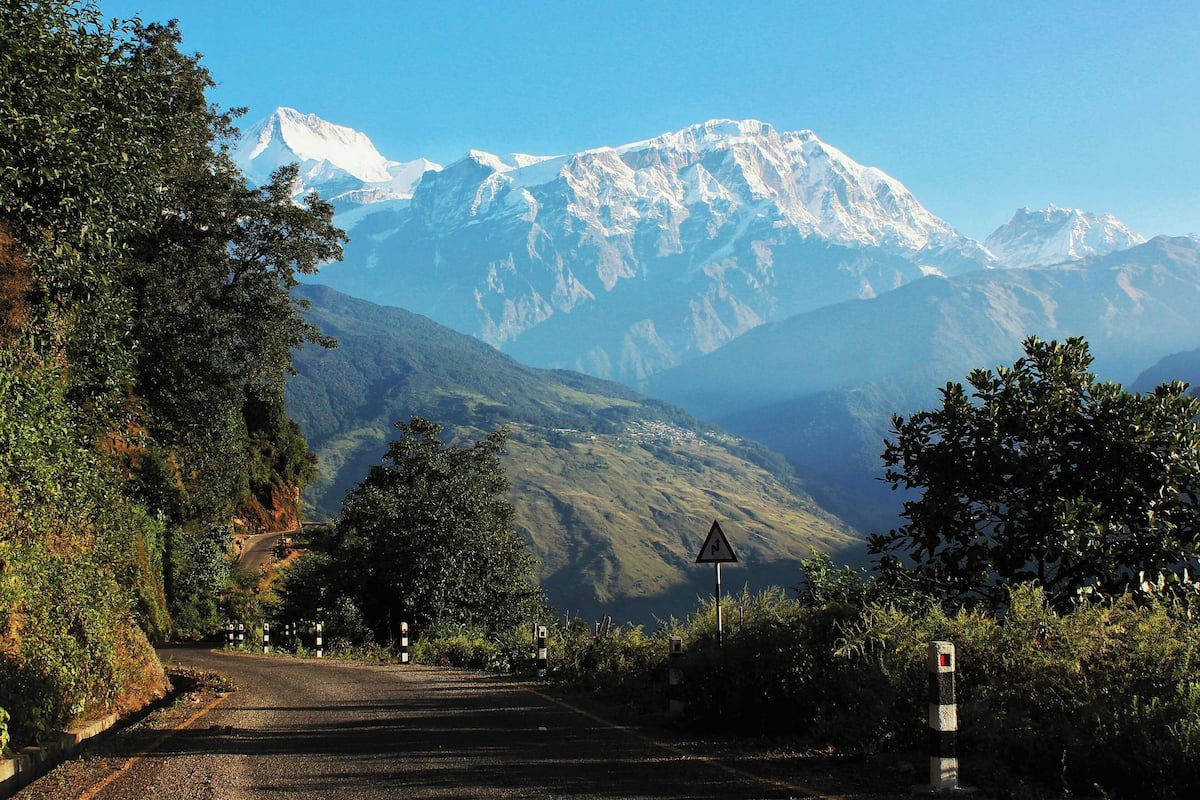 A road leading to a mountain range with a triangular warning sign.