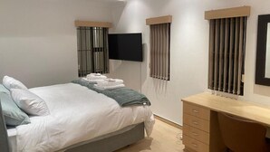 Une chambre à coucher moderne, équipée d’un lit, d’un bureau et d’une télévision.