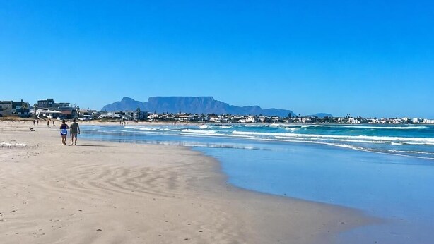 Une plage avec un ciel dégagé, une montagne en arrière-plan et quelques personnes qui se promènent.