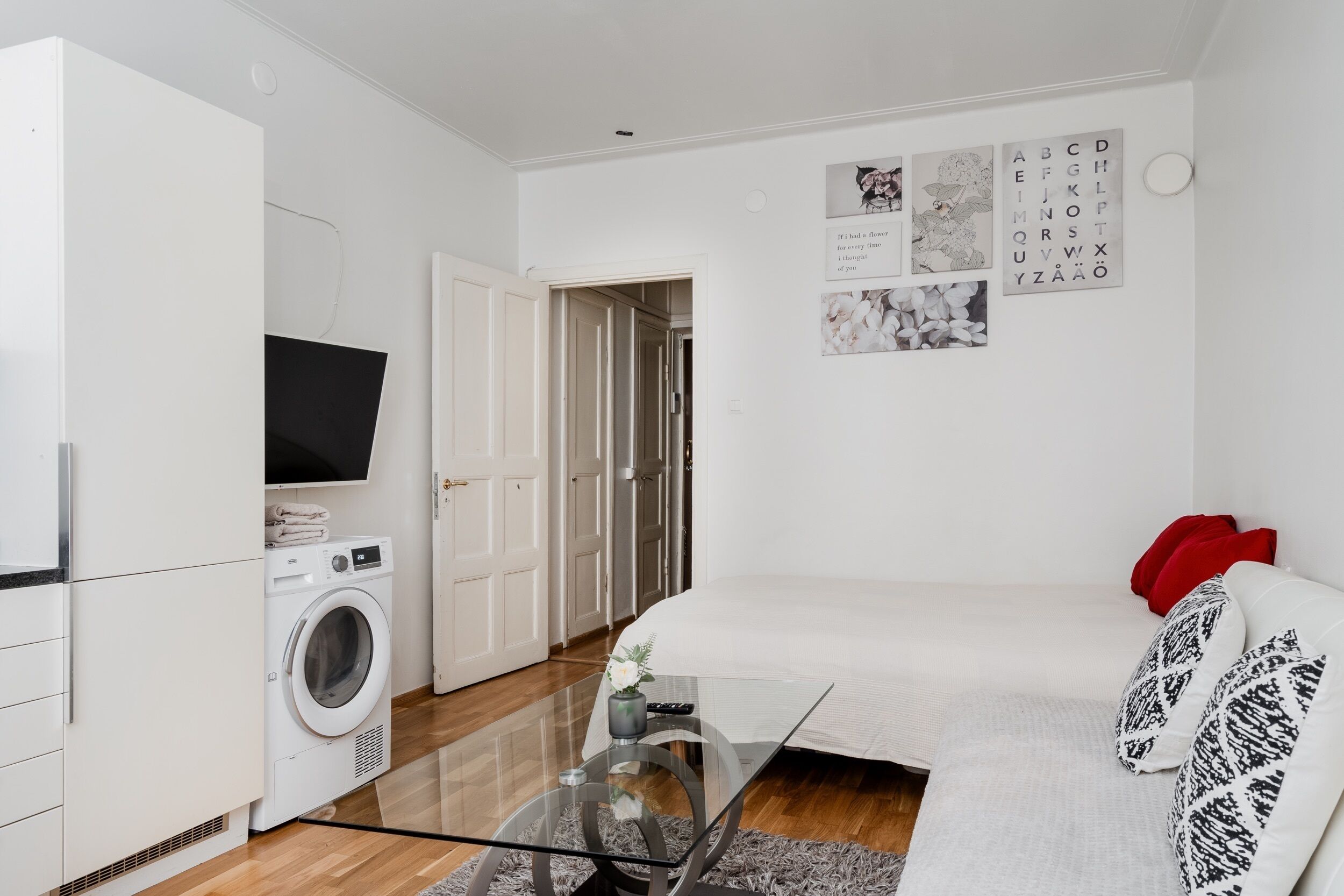 A compact living space with a washing machine, a flat-screen TV, a sofa, and a glass coffee table.