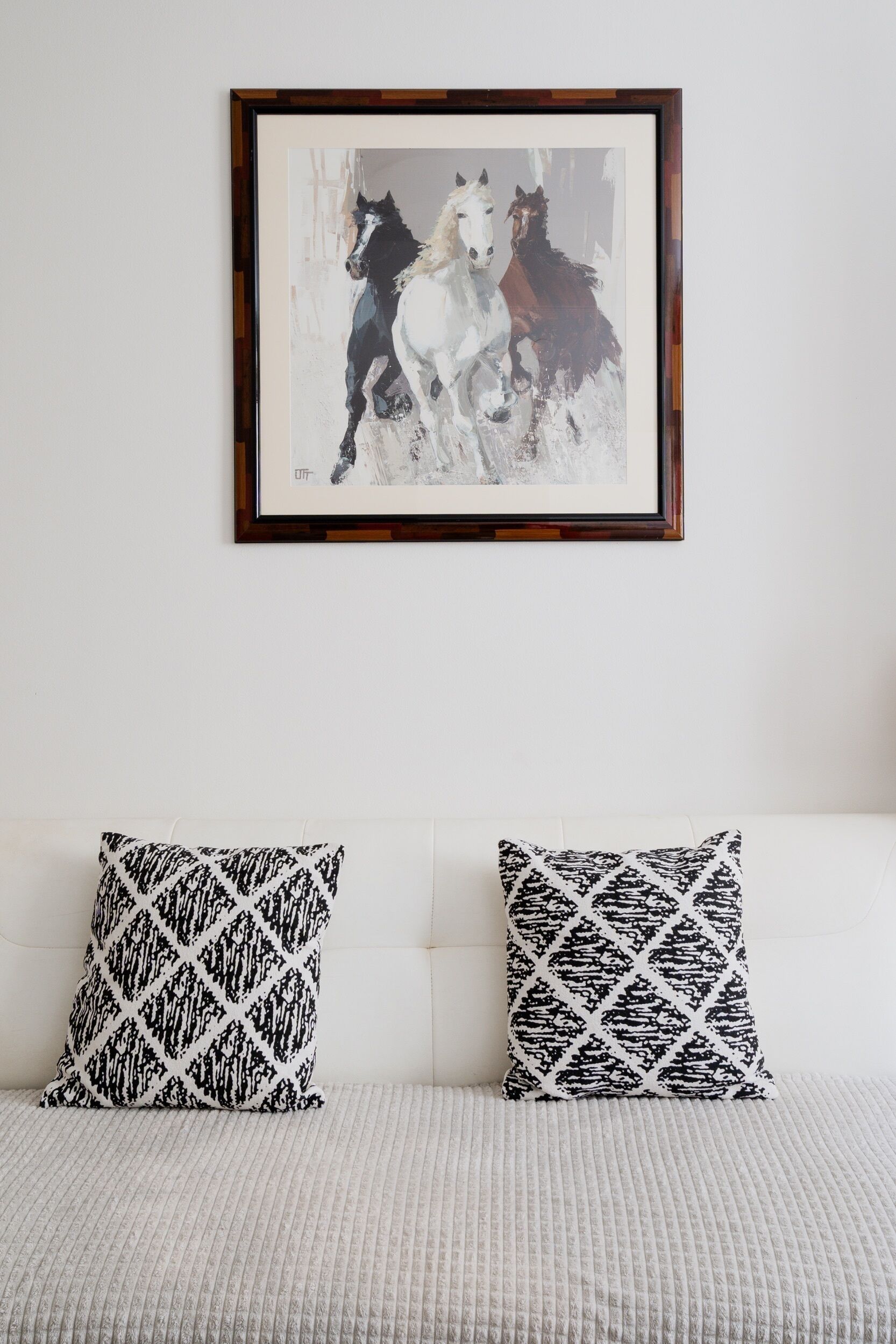 Un cuadro de caballos enmarcados en una pared, sobre un sofá blanco con almohadones estampados.