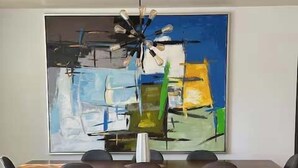 A dining area with a modern table, six chairs, a chandelier, and a large abstract painting on the wall.