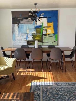 Ein Essbereich mit einem modernen Tisch, sechs Stühlen, einer Chandelierleuchte und einem großen abstrakten Gemälde an der Wand.