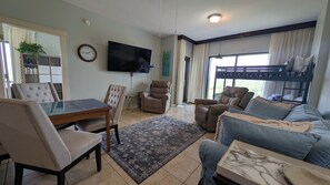 Ein Wohnzimmer mit Esstisch, zwei Stühlen, einer Couch, einem Liegesessel, einem Fernseher und einem Etagenbett.
