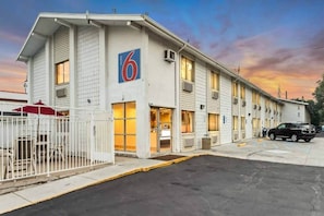 Un motel con un cartel grande con el número 6, una entrada con portón y un estacionamiento.