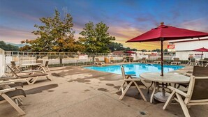 A pool area with lounge chairs and umbrellas, surrounded by a white fence.