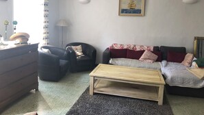 A living room with a sofa, armchairs, a coffee table, a lamp, and a painting on the wall.
