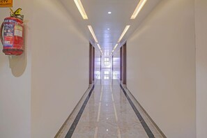 A corridor with a fire extinguisher mounted on the wall, recessed lighting, and a reflective floor. - Townhouse Skyboat XLO Point (Nashik)