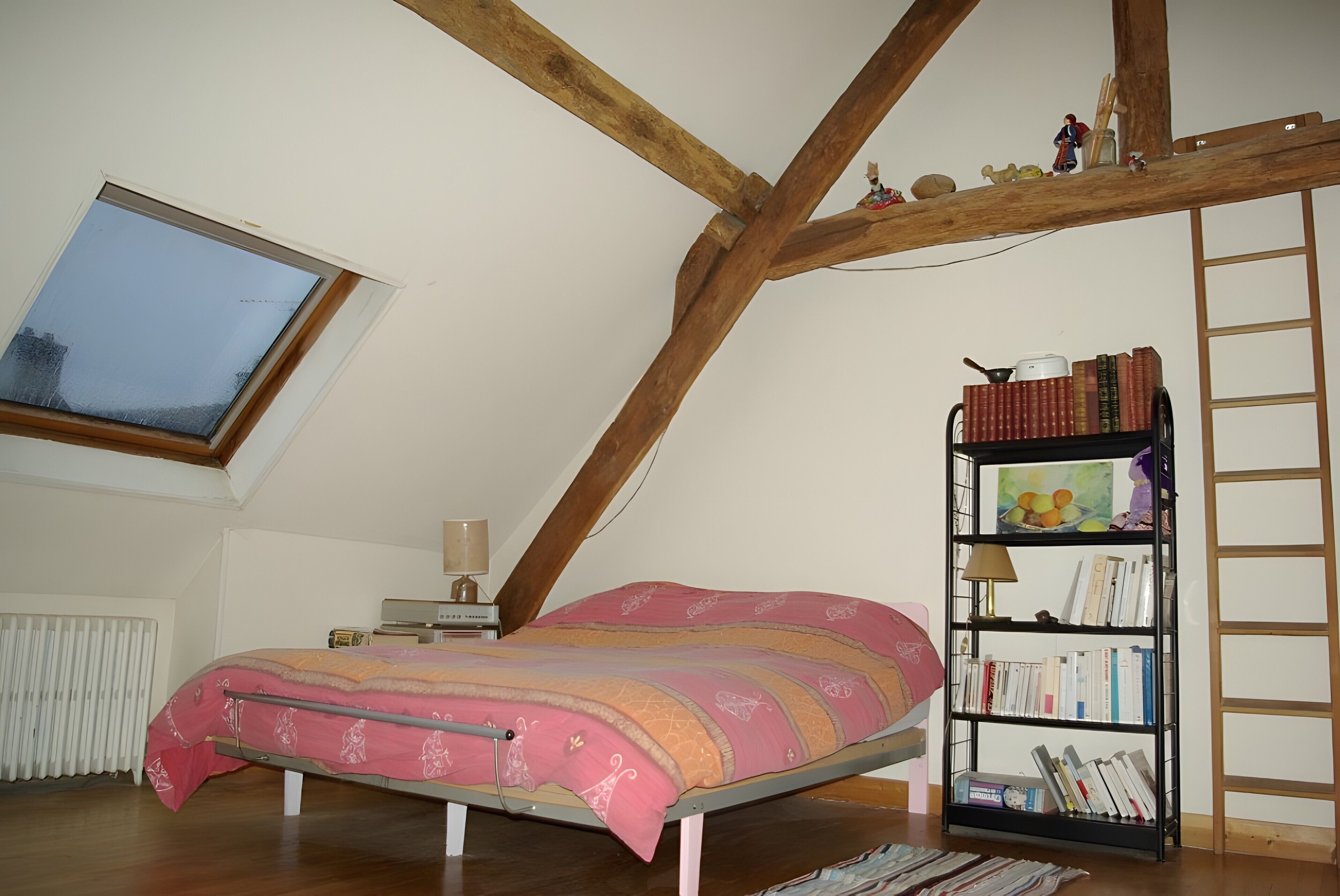 Ein Schlafzimmer mit schrägem Dach, einem Bett, einem Bücherregal und einem Fenster.