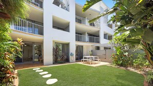 Un immeuble moderne à plusieurs étages, doté d’une pelouse bien entretenue et d’un espace extérieur aménagé avec des sièges.