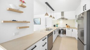 Une cuisine moderne dotée d’étagères en bois, de luminaires suspendus, d’un réfrigérateur en acier inoxydable et d’un lave-vaisselle.