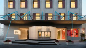 Un edificio moderno con una entrada curva, numerosas ventanas y una escalera con barandillas azules.