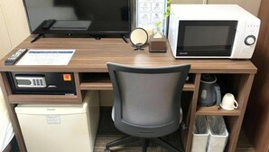 Habitación de hotel con escritorio de madera, televisor, microondas, refrigerador, una silla y cafetera.