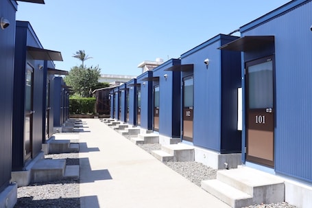 A row of blue hotel rooms with numbered doors, a concrete pathway, and a clear sky.