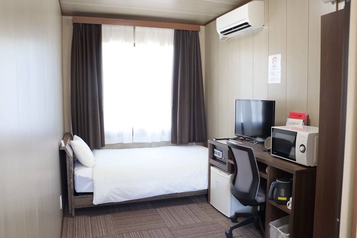 Habitación de hotel con una cama, un escritorio con computadora y microondas, y un equipo de aire acondicionado.