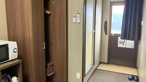 Habitación de hotel con armario, microondas, zapatero y una puerta con ventanal.