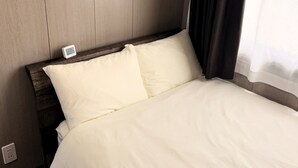 Una cama con ropa de cama blanca, un cabecero de madera y una mesita de noche con un reloj.