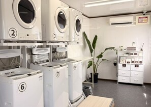 Un cuarto de lavandería con lavadoras y secadoras numeradas, una planta en maceta y un armario de almacenamiento.