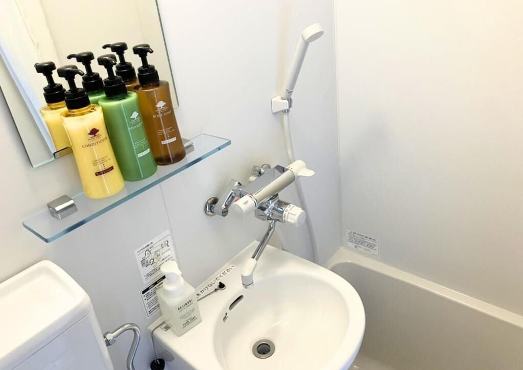 Un baño con lavamanos blanco, repisa de vidrio con artículos de aseo, y ducha de mano.