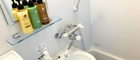 Un baño con lavamanos blanco, repisa de vidrio con artículos de aseo, y ducha de mano.