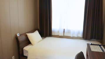 Quarto de hotel com cama, escrivaninha e janela com cortinas.