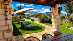 A covered outdoor seating area with stone walls, a pool, and a mountainous backdrop. - Hidden Oasis Amazing Seaview - Kalisti 1BD 1BA 4PL (Kokkino Chorio city)