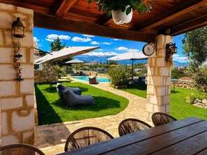 A covered outdoor seating area with stone walls, a pool, and a mountainous backdrop. - Hidden Oasis Amazing Seaview - Kalisti 1BD 1BA 4PL (Kokkino Chorio city)
