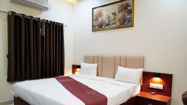 A neatly made bed with a headboard, two bedside tables with lamps, a painting on the wall, and a window with curtains. - Perfect 5-bedroom hotel with AC in pleasant Varanasi (Varanasi)