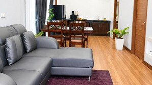 A modern living room with a grey sofa, a dining table with chairs, a kitchen area, and a wooden door. - Villa Escape , Aonang Krabi (Meung krabi)