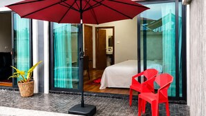 A modern hotel room with a glass door leading to a balcony, a red umbrella, and a pool area. - Villa Escape , Aonang Krabi (Meung krabi)