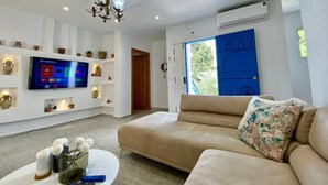 Ein modernes Wohnzimmer mit einem beigen Sofa, einem wandmontierten Fernseher und einer Wand mit Regalen.