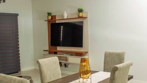Una zona de menjador amb un televisor penjat a la paret, una taula de fusta i quatre cadires.