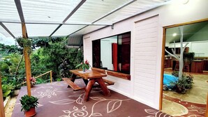 A covered patio with a wooden table and benches, surrounded by potted plants and a decorative floor pattern. - Peaceful family house Destiny Homes (Pocosol)